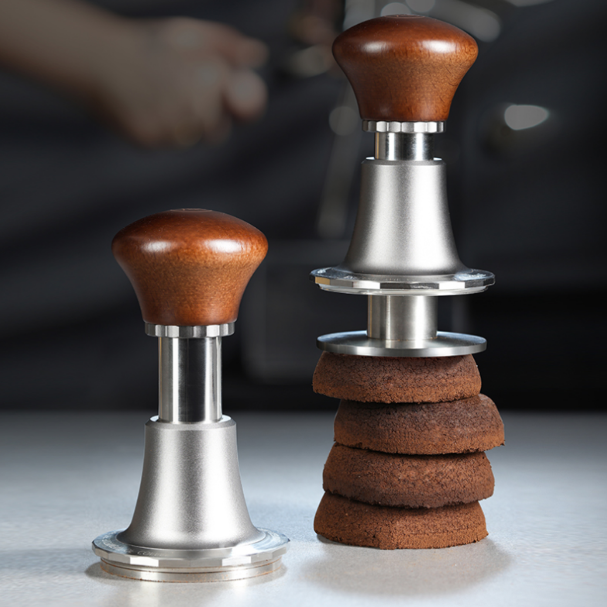  Adjustable espresso tamper with ergonomic wooden handle and stainless steel base, demonstrating even coffee puck compression with stacked used coffee pucks.