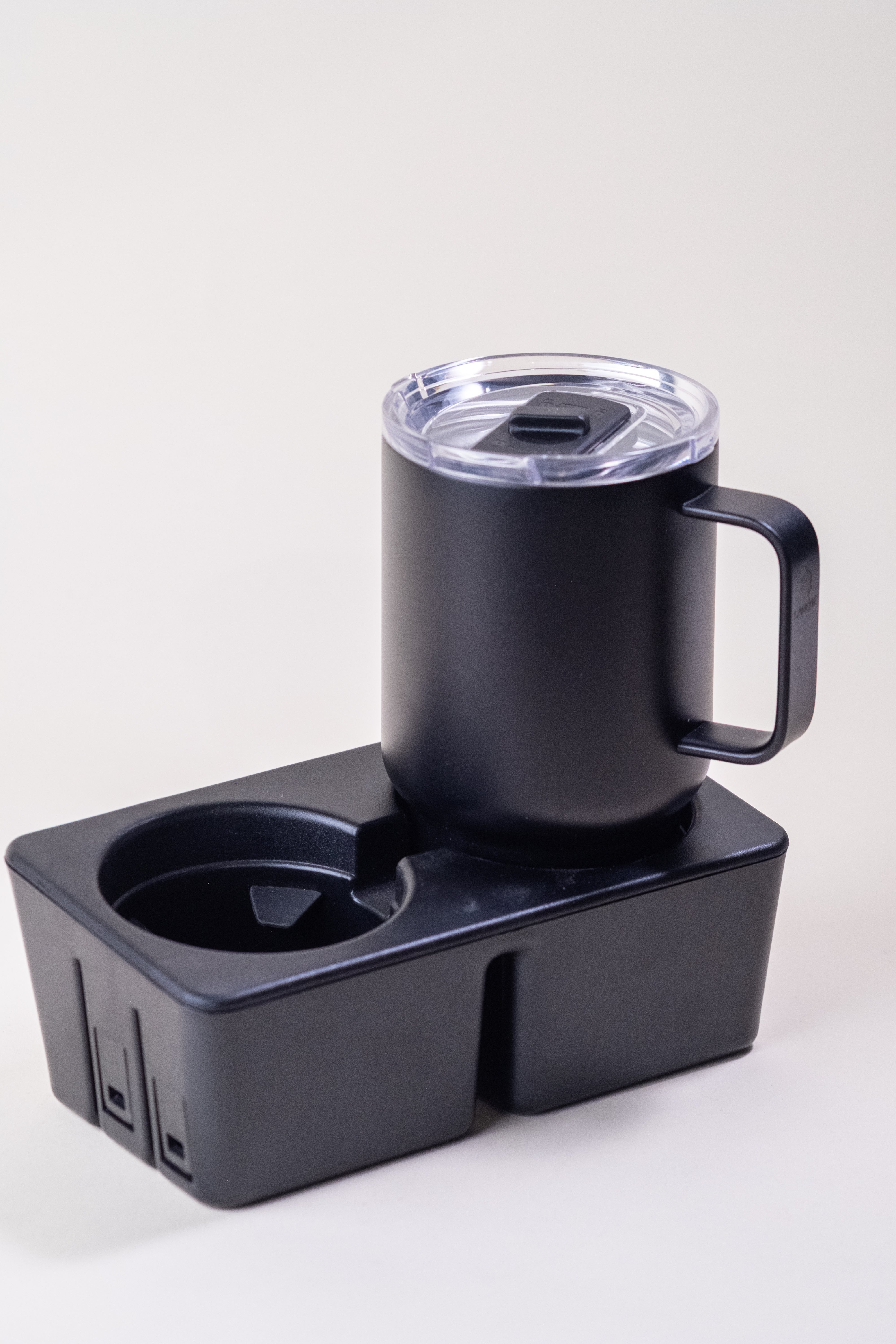 Black insulated coffee mug with a sturdy handle and clear spill-resistant lid, placed on a black organizer with a cup holder. Stainless steel design for hot and cold beverages.