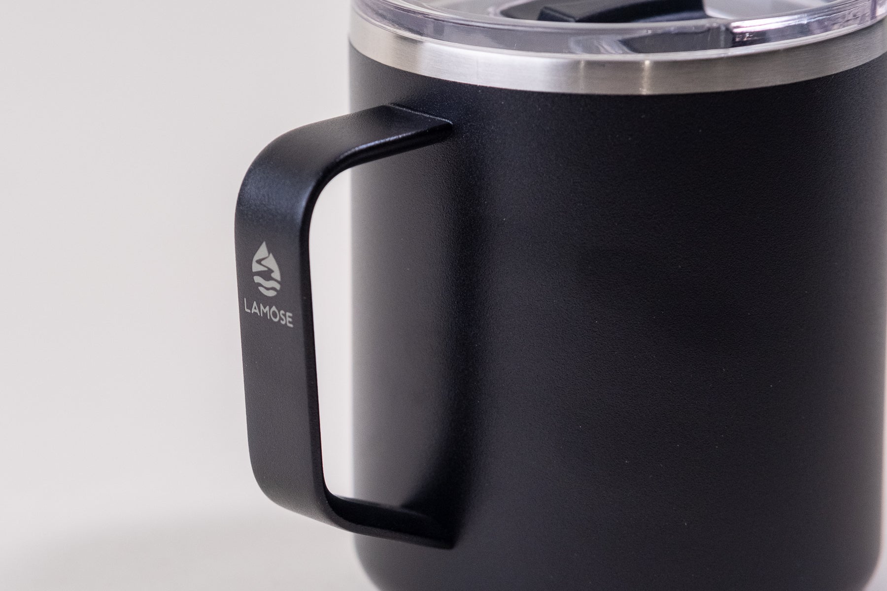 Close-up of a black insulated coffee mug handle with a Lamose logo. Stainless steel mug with a sturdy grip and spill-resistant lid, designed for hot and cold beverages.