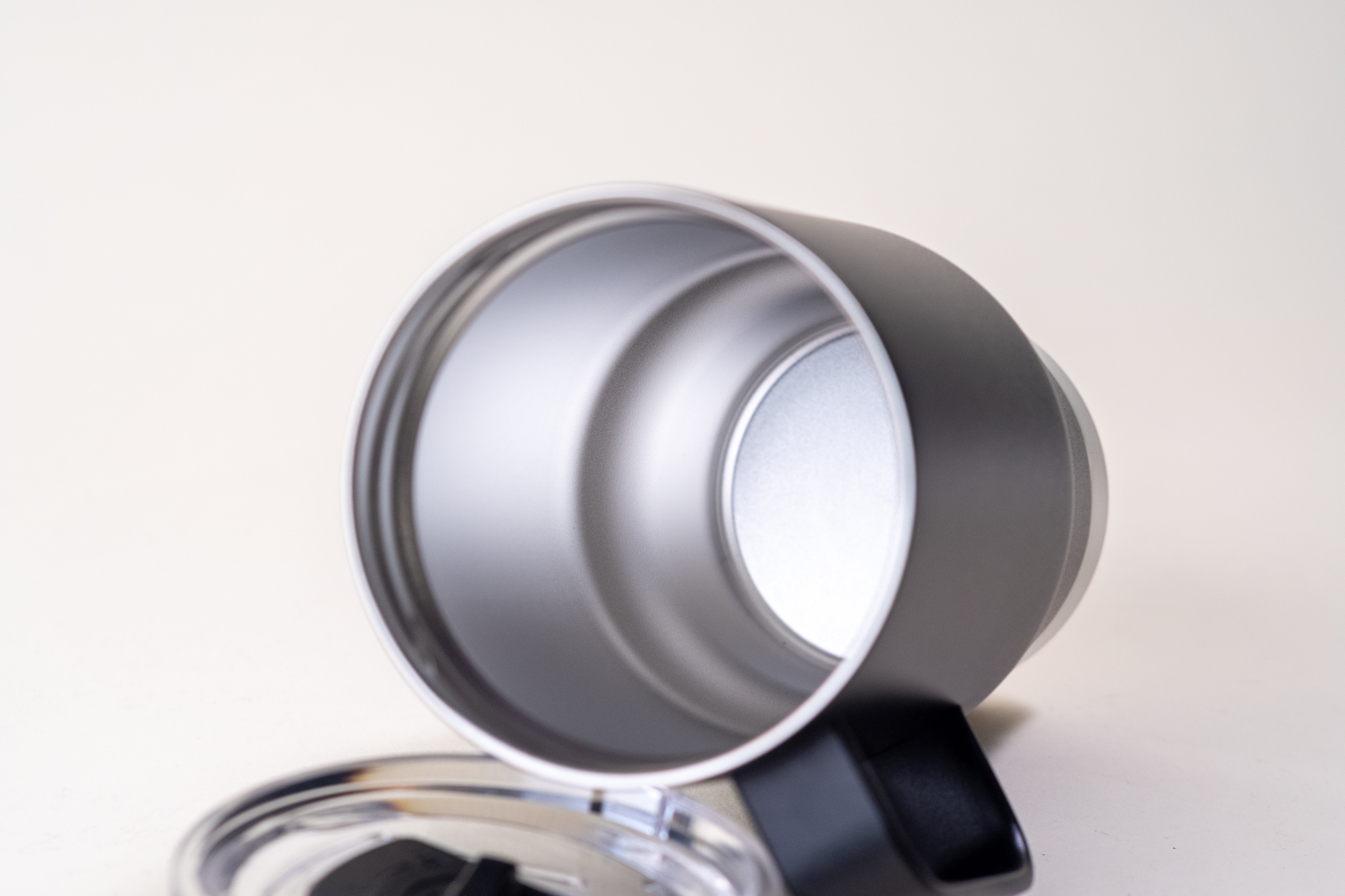 Close-up of the interior of a black insulated coffee mug with a stainless steel double-wall design for heat retention. Includes a clear spill-resistant lid, shown beside the mug.