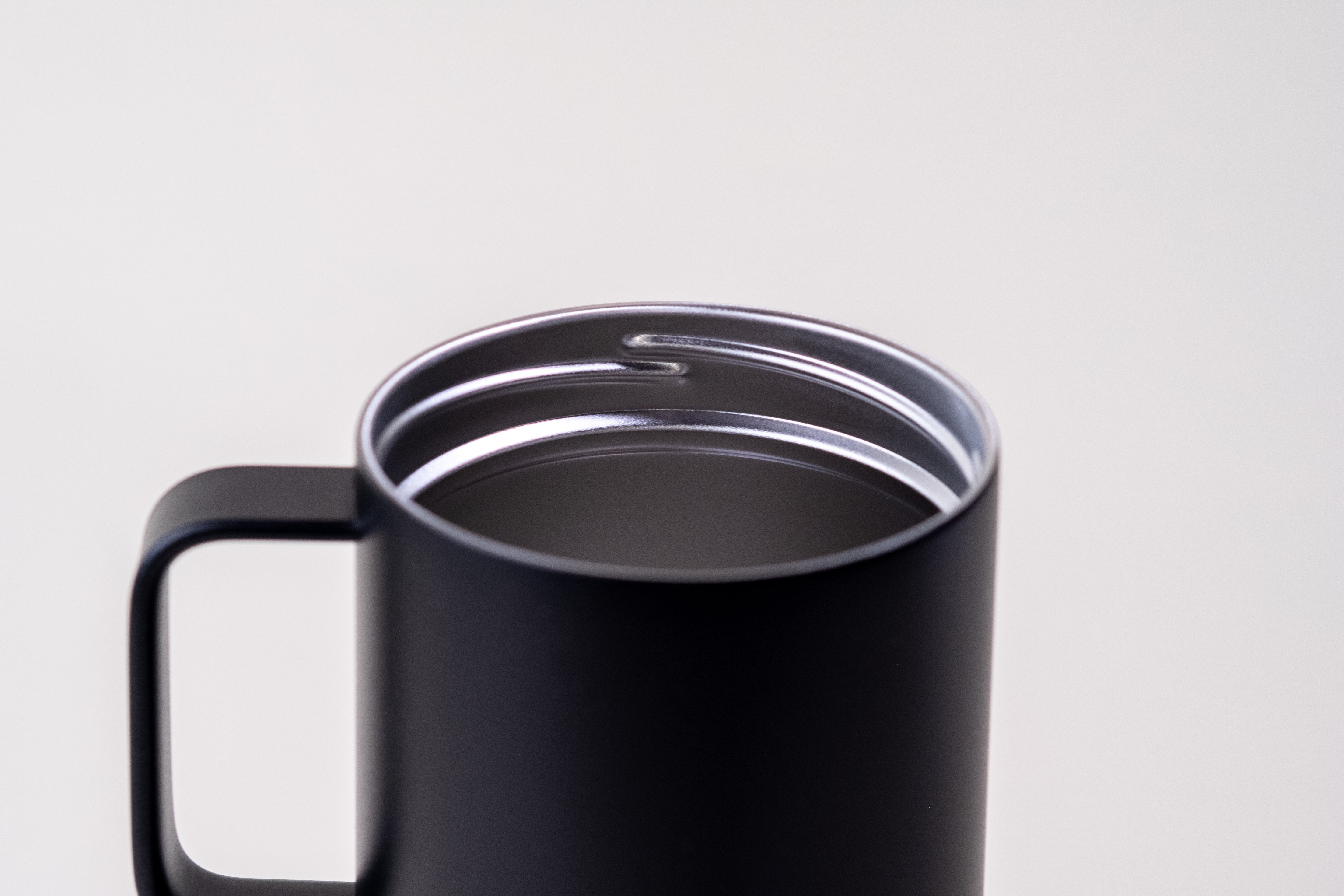 Close-up view of a black insulated coffee mug with a sturdy handle and stainless steel double-wall interior for heat retention. Designed for hot and cold beverages.