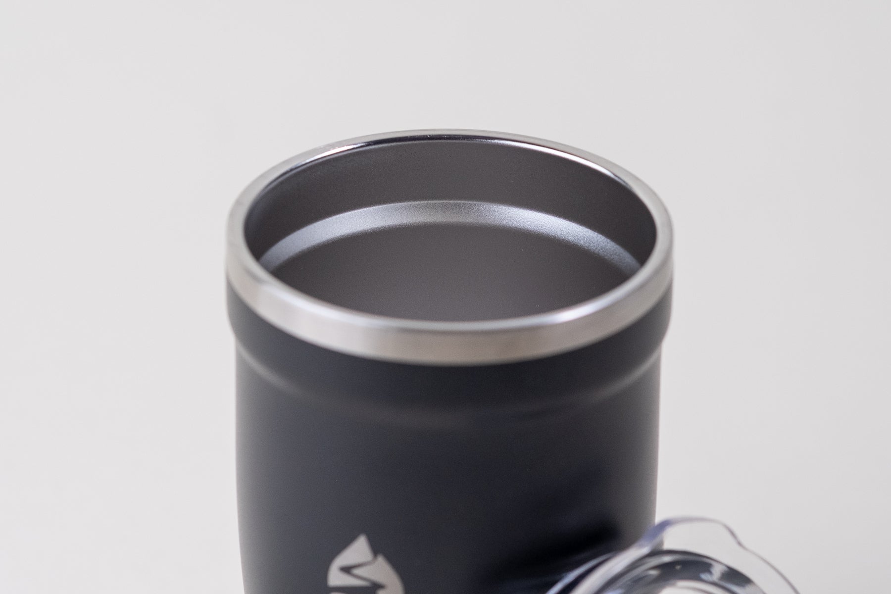 Close-up of a black insulated tumbler with a stainless steel rim and a smooth interior. Includes a removable clear spill-resistant lid, ideal for hot and cold beverages.