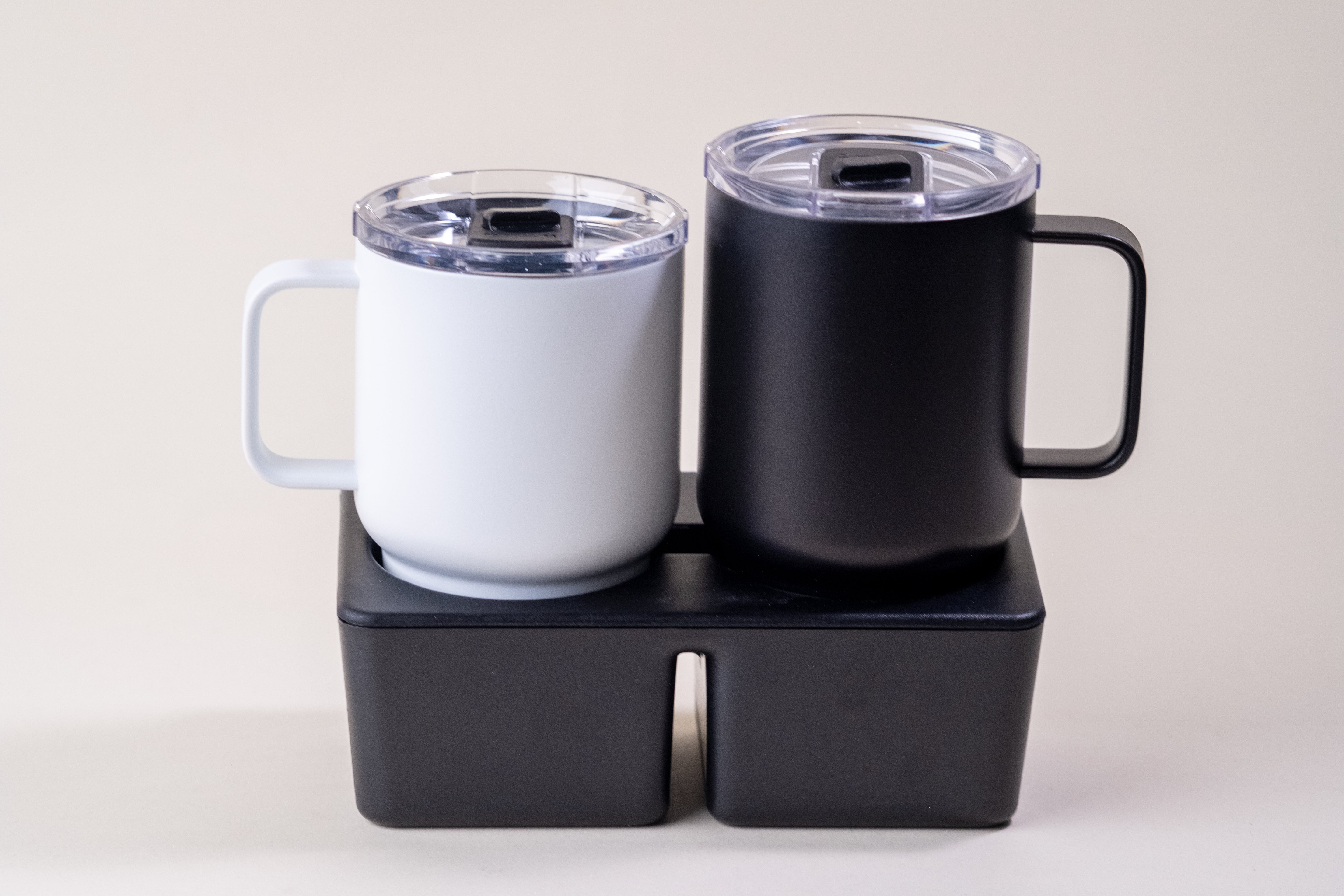 Black and white insulated coffee mugs with spill-proof lids, securely placed in a dual cupholder. Stainless steel design for hot and cold drinks.