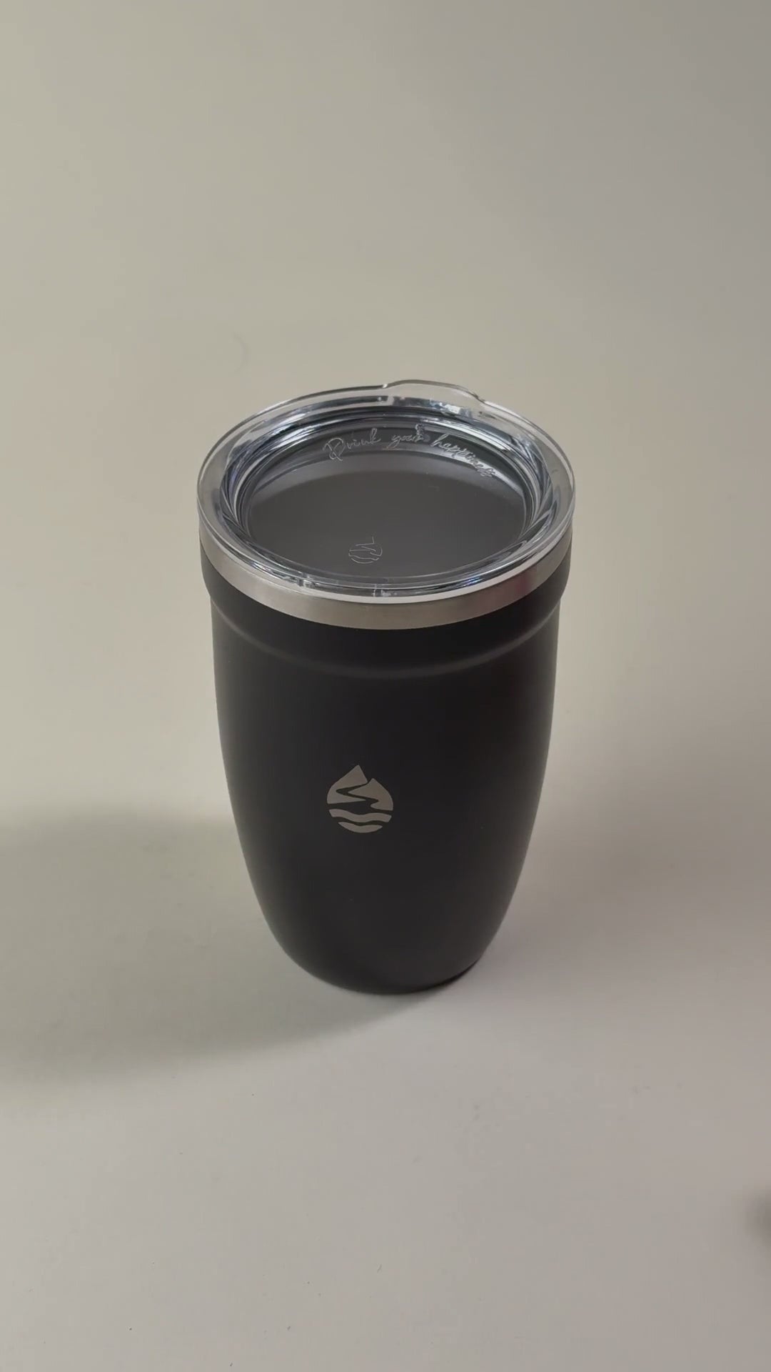 Load video: Hand holding an open black insulated tumbler with a stainless steel interior and a removed clear spill-resistant lid. Double-wall vacuum design for hot and cold beverages.