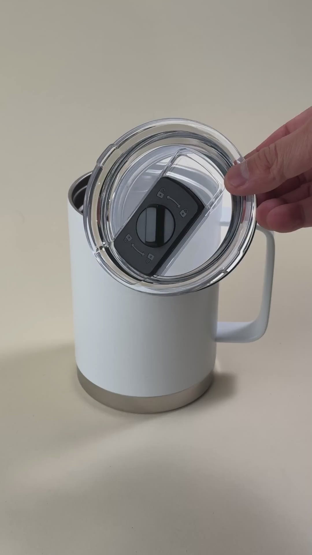 Load video: White insulated travel mug with a stainless steel base, featuring a spill-proof, sliding-lock lid being held by a hand.