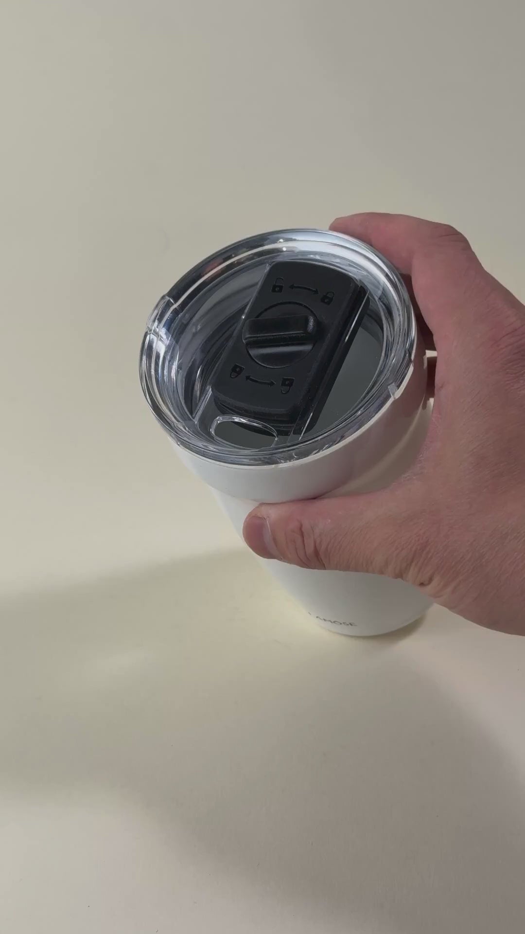 Load video: Hand adjusting the sliding lock mechanism on a white insulated tumbler with a clear spill-resistant lid. Stainless steel travel mug designed for hot and cold beverages.