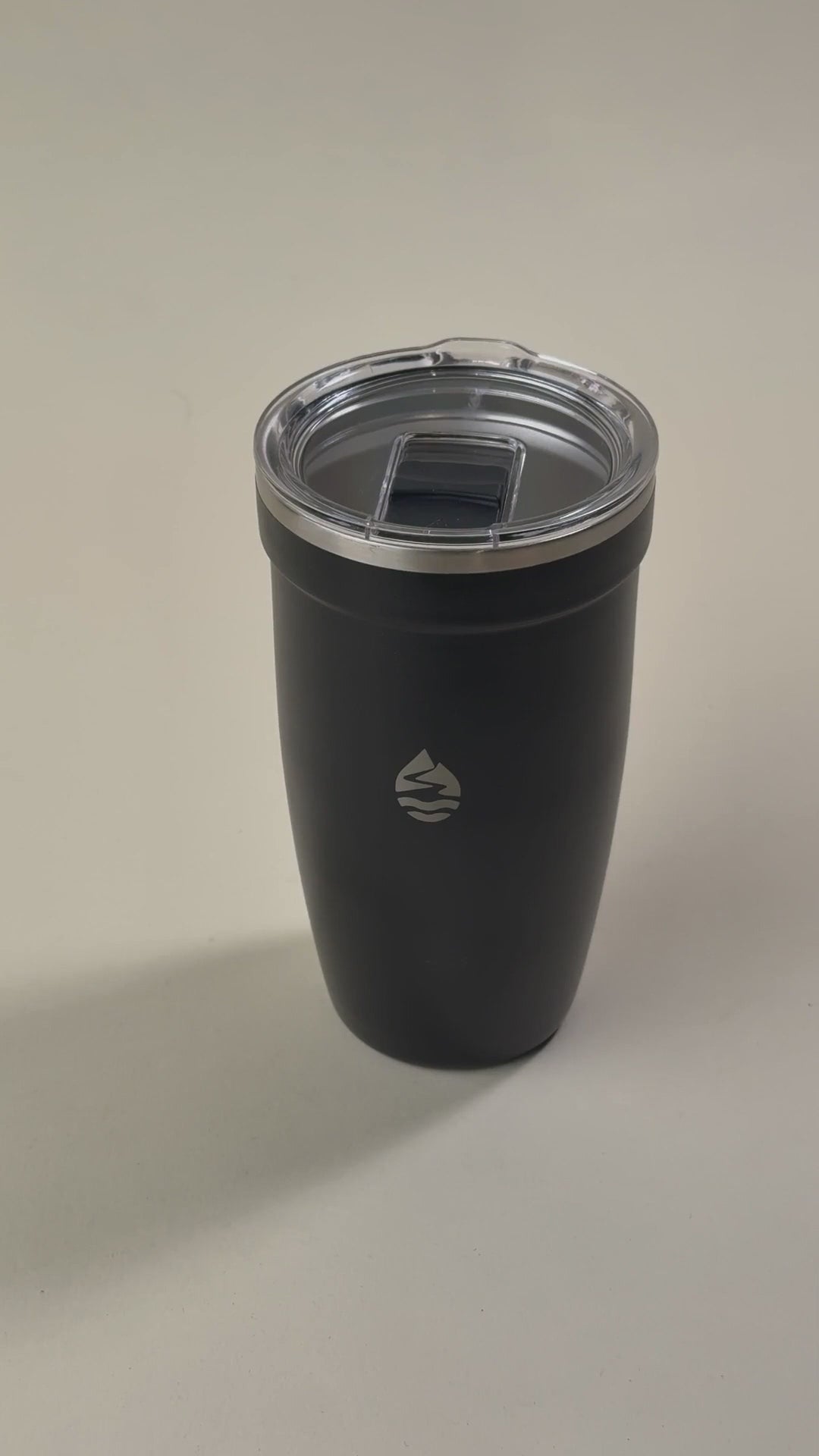 Load video: Sleek black insulated tumbler with a spill-resistant clear lid, featuring a minimalist engraved logo for a modern and stylish look.