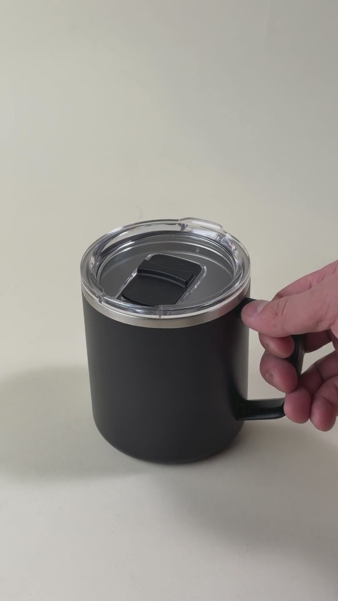 Load video: Black insulated coffee mug with a clear spill-resistant lid. Stainless steel mug with a handle, perfect for hot and cold beverages, featuring a secure sliding closure.