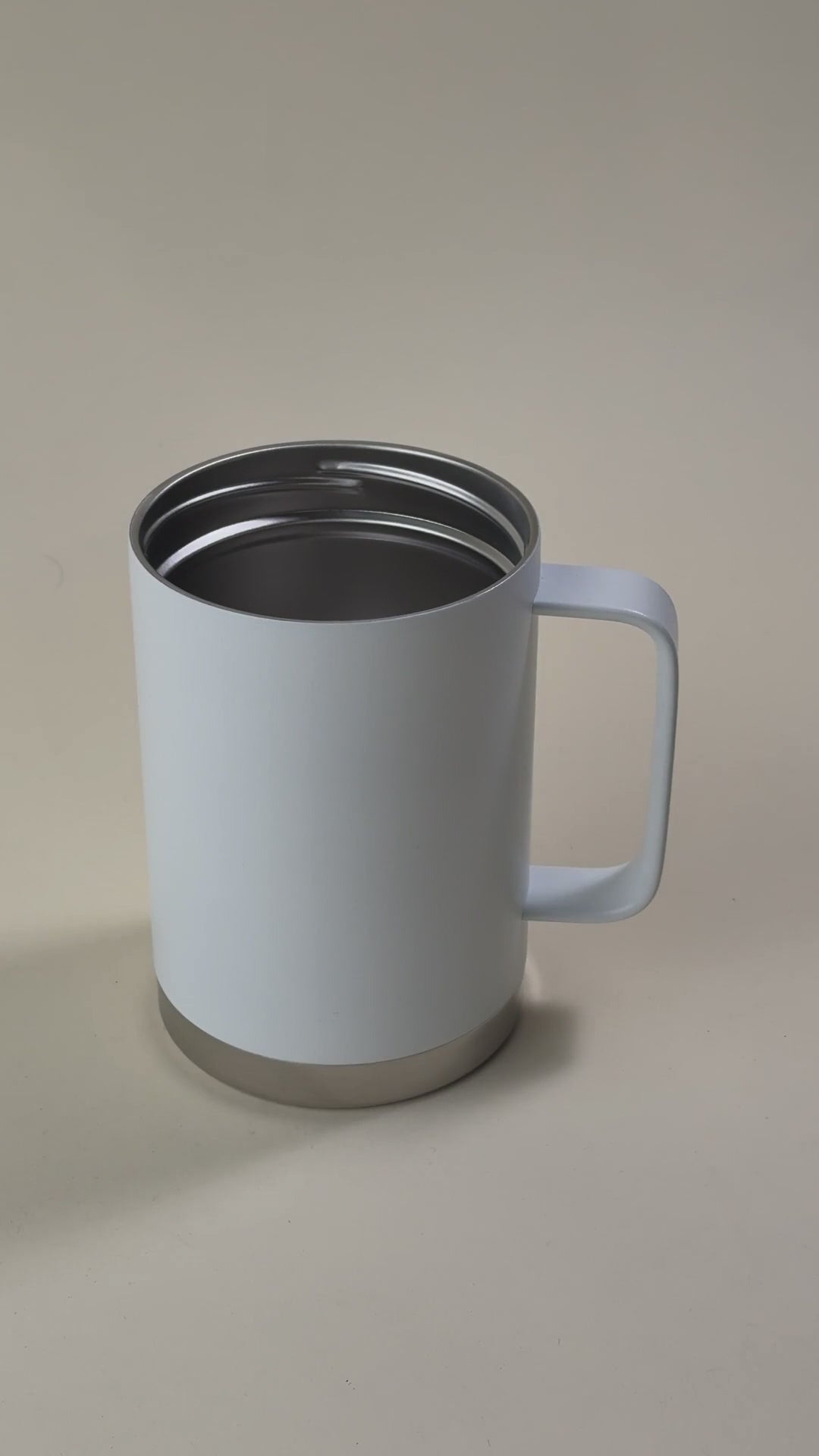 Load video: White insulated travel mug with a stainless steel base, featuring a spill-proof, sliding-lock lid being held by a hand.