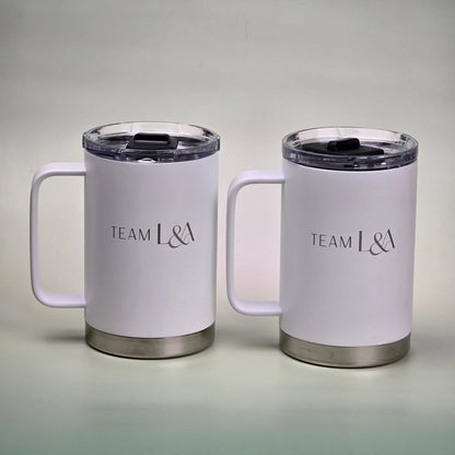 Pair of white insulated mugs with custom silver engraving that reads 'Team L&A,' featuring stainless steel bases and black spill-proof lids.
