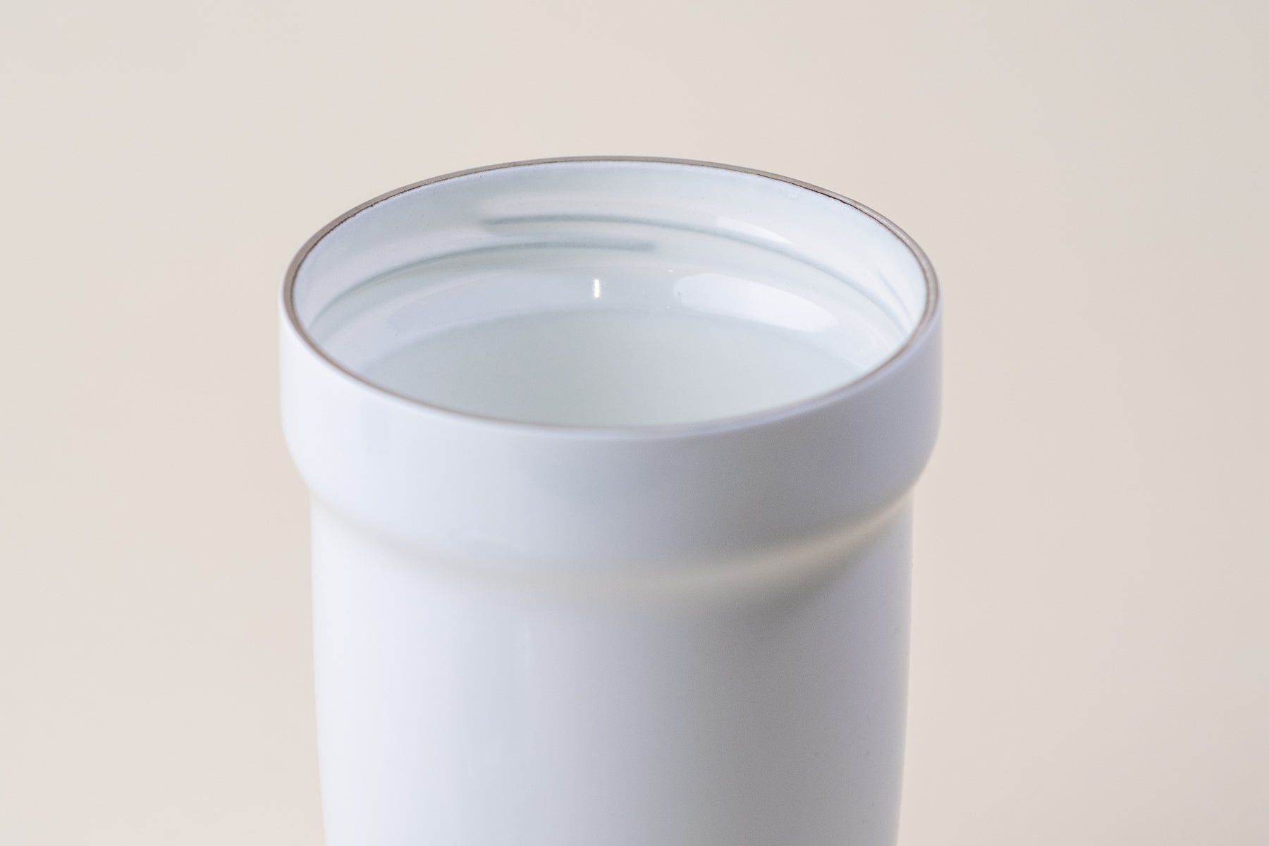 Close-up view of the interior of a white enamel-coated insulated tumbler, showcasing its smooth finish and durable design for hot and cold beverages