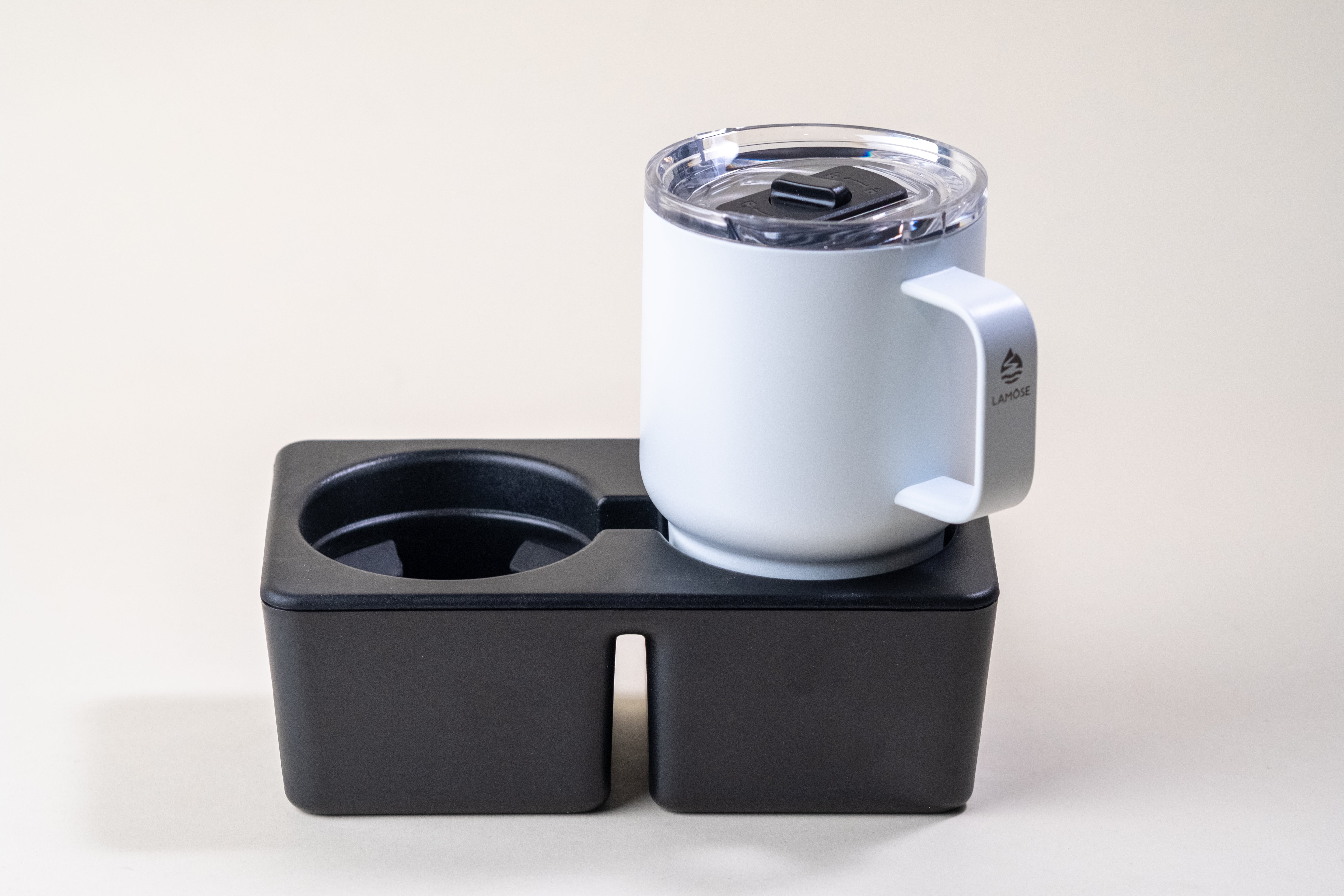 White insulated coffee mug with a secure lid, placed in a black dual cupholder organizer for car use.