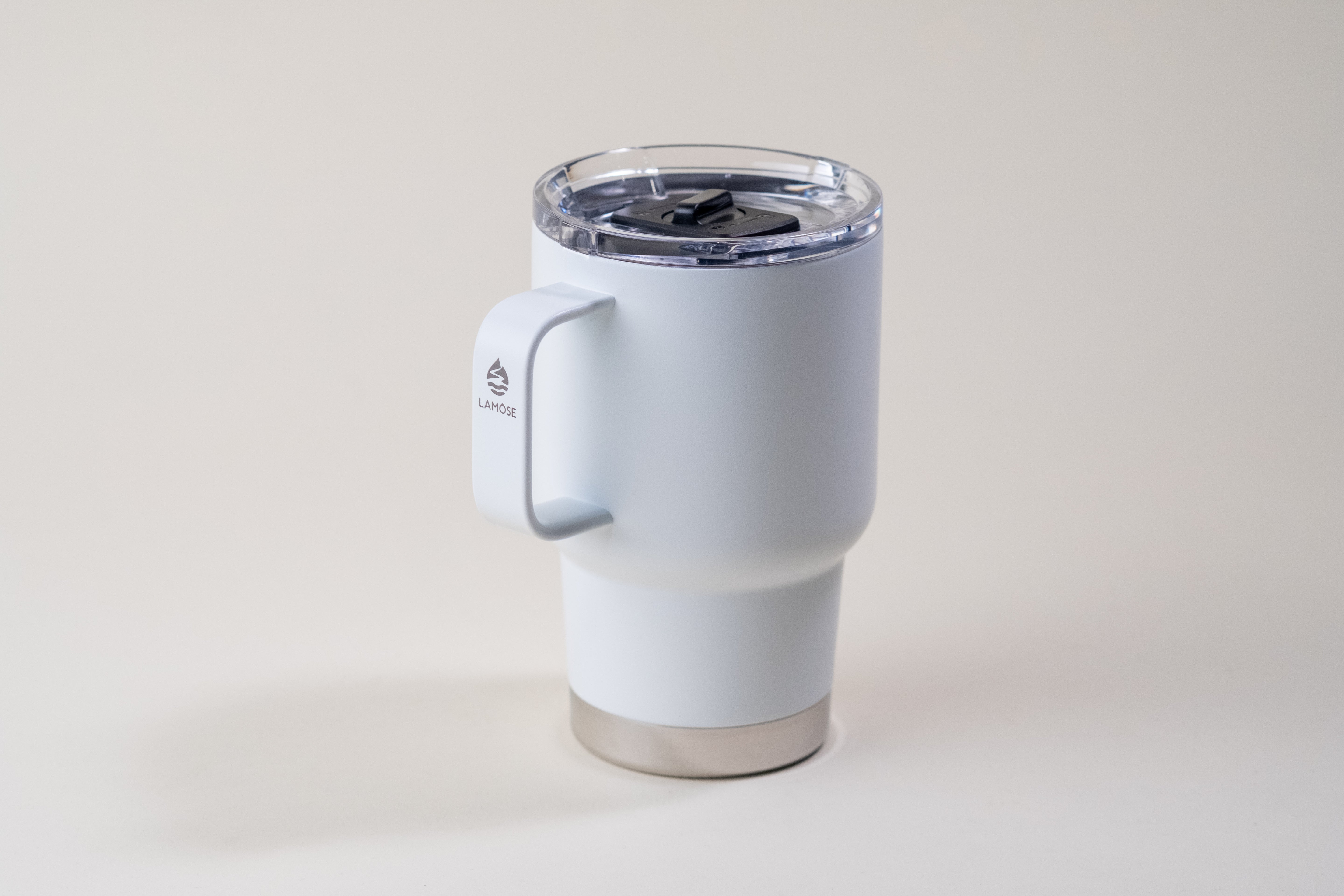 White insulated travel mug with ergonomic handle, clear sliding lid, and stainless steel base, featuring the Lamose logo.